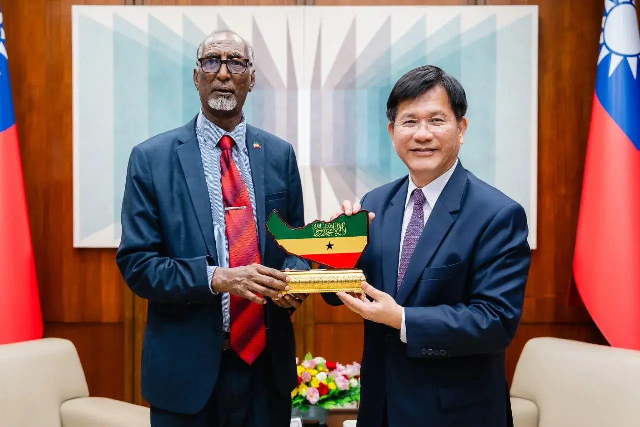 Two officials hold a commemorative plaque in the shape of Somaliland, in a meeting room hung with Taiwan flags